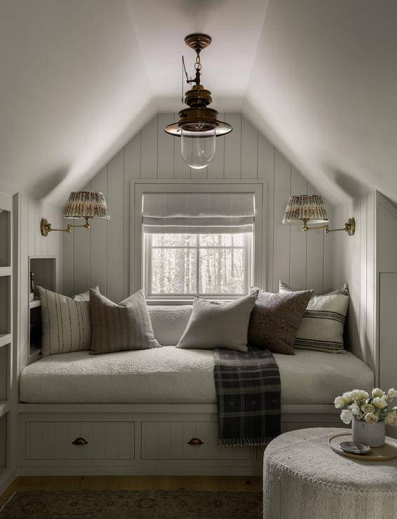 Attic nook features a built in reading bench with gray cushions and drawers accented with brass cup pulls and gray vertical shiplap trim illuminated by a vintage brass lantern.