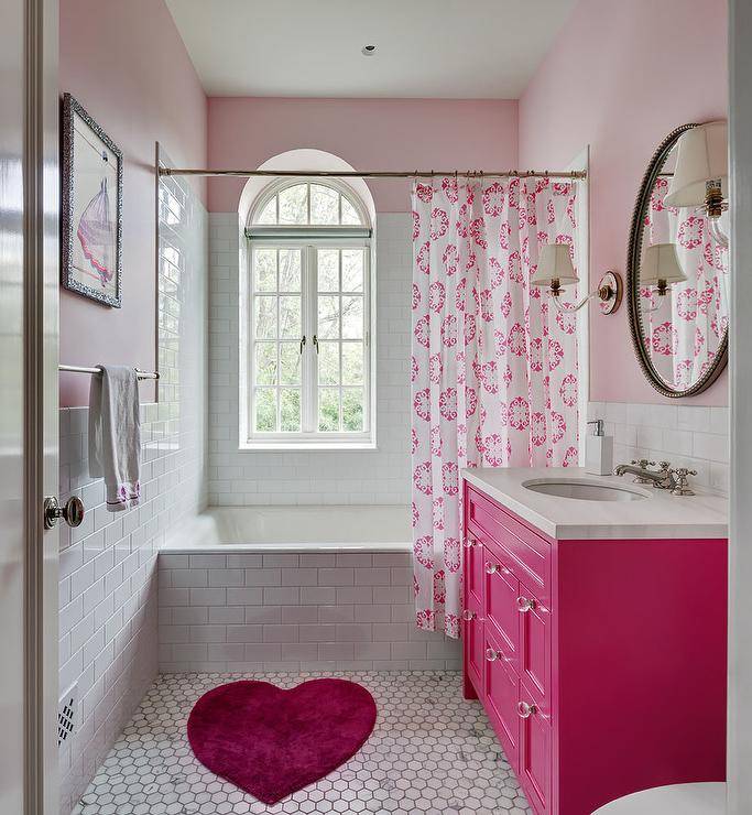 pink girl's bathroom features a pink heart shaped bath rug placed on white and pink  honeycomb floor tiles in front of a hot pink washstand accented by pink and white shower curtain