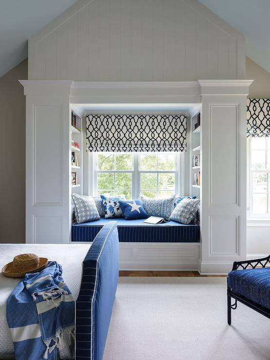 Boy's room features a window seat reading nook with a blue striped cushion and blue pillows under a black and white trellis Roman shade and a blue bed.