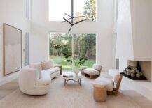 Modern living room features a white boucle curved sofa with round marble top coffee table, a modern fireplace design and low wood and fabric accent chairs atop a light brown jute rug.