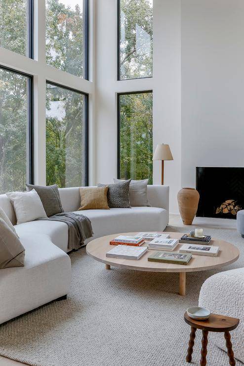 A curved white sofa topped with gray and brown pillows is placed in front of windows at a round low coffee table.