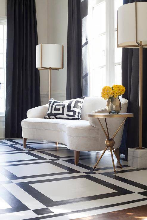 Clad in black and white geometric floor tiles, this stunning dining room features a Mitc، Gold + Bob Williams Vera Sofa topped with a black and white pillow and positioned beside a marble and br، accent table in front of a window dressed in black curtains lit by Arteriors Pearson Floor Lamps.