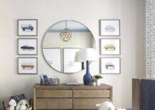 Blue crown molding frames a blue agate wallpapered ceiling in a beautiful nursery featuring vintage car prints hung flanking a round mirror fixed over a brown wooden dresser lit by a blue lamp.