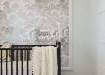 Modern boy's nursery features a horse mobile over a black nursery crib against a wall clad in Fornasetti Nuvole framed cloud wallpaper.