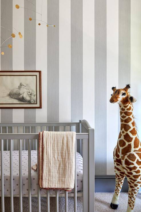 Boy's nursery features a gray crib on gray vertical stripe wallpaper and a tall stuffed giraffe.