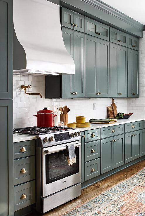 Transitional kitchen with mixed metals boasts a cooktop with a stainless steel vent hood and an antique brass pot filler on white subway tiles for a timeless appeal.