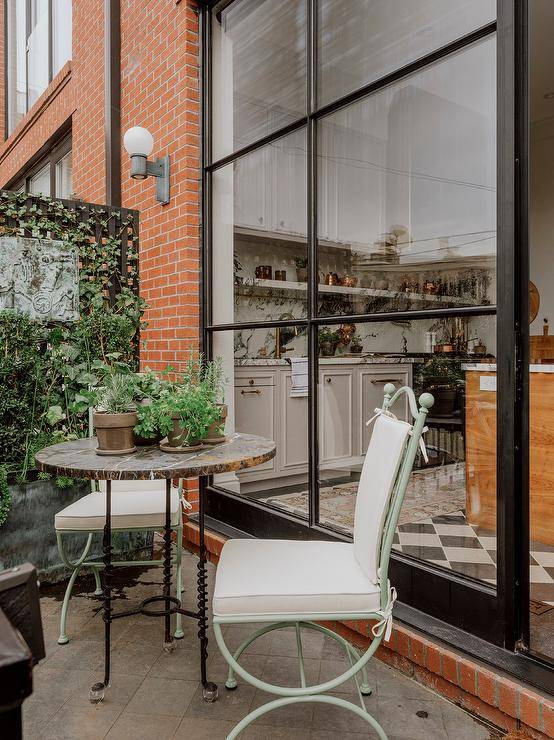 Mint green wrought iron chairs with white cushions are placed on a French style balconette at a marble bistro table.