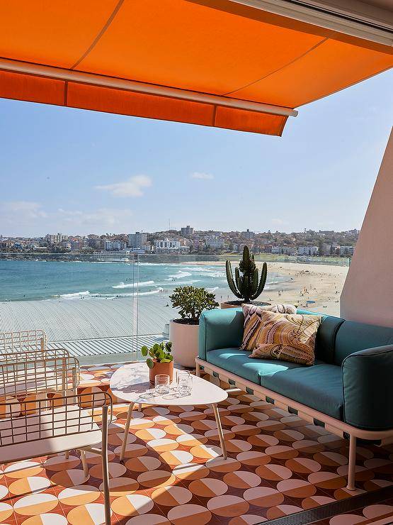Balcony features orange and yellow mosaic floor tiles, a marble top coffee table and a turquoise blue sofa under an orange awning.