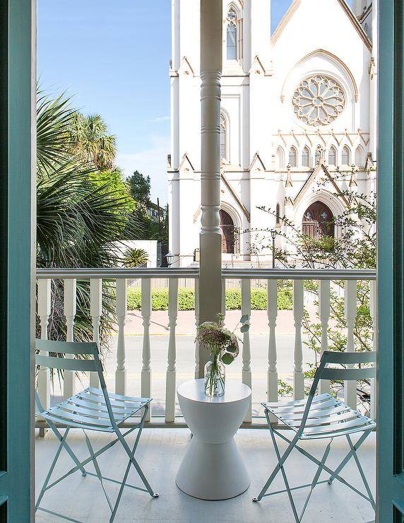 Chic balcony is filled with blue slatted folding chairs and a white hourglass accent table.