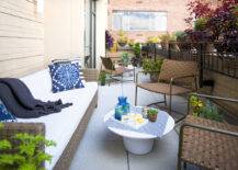 Private apartment terrace features outdoor woven sofa topped with white seat cushions, indigo blue pillows and a dark navy tasseled throw across from a pair of metal framed woven leather chairs alongside a modern round white coffee table.