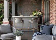 Beautifully styled covered patio bar features gray and gold barstools placed at a gray bar island with a marble countertop.