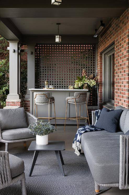 Beautifully styled covered patio bar features gray and gold barstools placed at a gray bar island with a marble countertop.