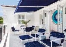 Under a navy blue balcony awning, navy blue basketweave chairs with matching stools are topped with blue stripe lumbar pillows and navy blue basketweave dining chairs surround a white dining table.
