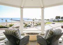 With a beautiful beach view, Candelabra Home Loom Arm Chairs sit on a bedroom balcony facing a round concrete fire pit.