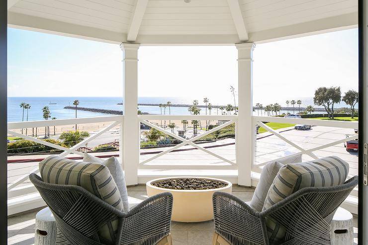 With a beautiful beach view, Candelabra Home Loom Arm Chairs sit on a bedroom balcony facing a round concrete fire pit.