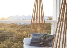 Chic covered second floor balcony is fitted with a rope swing bed adorned with plush white cushions and blue striped pillows.