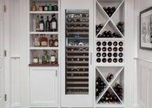 Basement with built-in wine racks and white cabinets finished with nickel hardware storing wine and beverages and spirits. This custom basement wine room features a tall wine fridge centered between shelves.