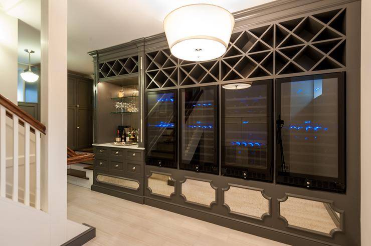 Built-in wine racks over side by side wine coolers in a dark gray basement built-in. Stunning built-in accents include mirrored panels, glass front wine cooler doors, and x trim shelves.