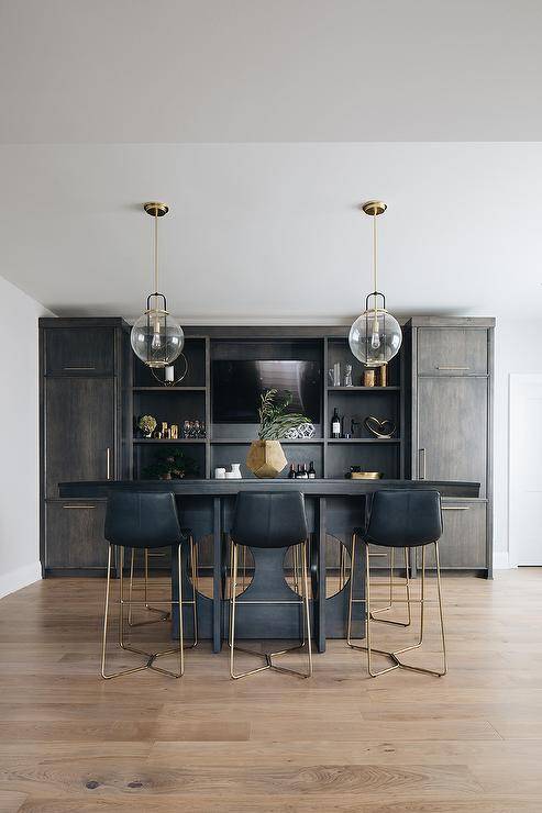 Black leather stools at a basement bar features gold base complimenting brass and clear globe pendant lights.