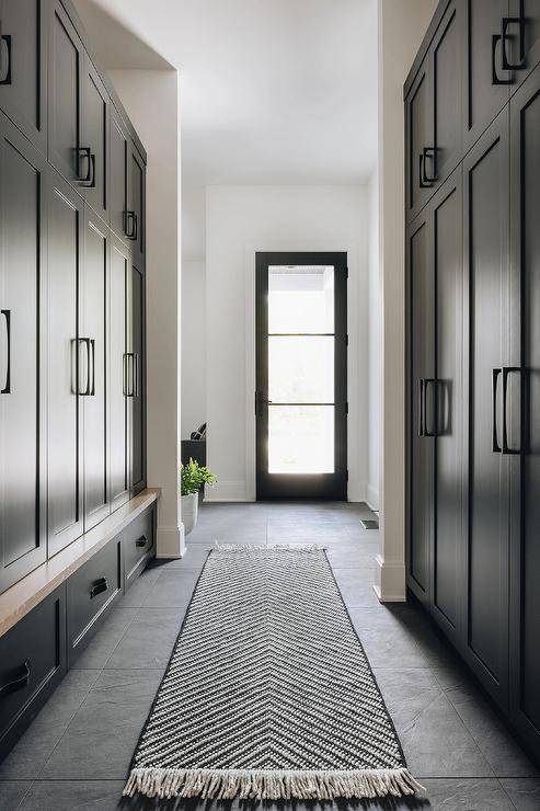 A black chevron runner sits on black floor tiles in a black galley-style mudroom between facing closed black lockers finished with matte black hardware.