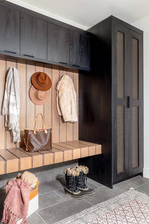 Mudroom features a floating oak bench under hooks with black oak cabinets and a pink and gray mudroom rug.