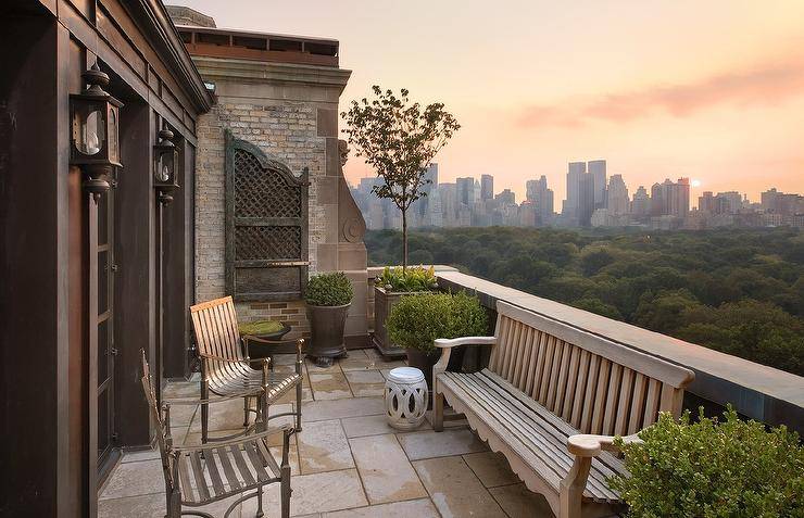 Chic balcony features a teak bench facing a pair of wrought iron chairs.