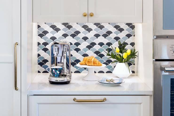 Kitchen coffee station features blue and black scale tiles and white cabinets accented with brass pulls.