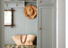 Cottage style mudroom features a built in gray mudroom bench and cabinets with beadboard trim and vintage brass hardware.