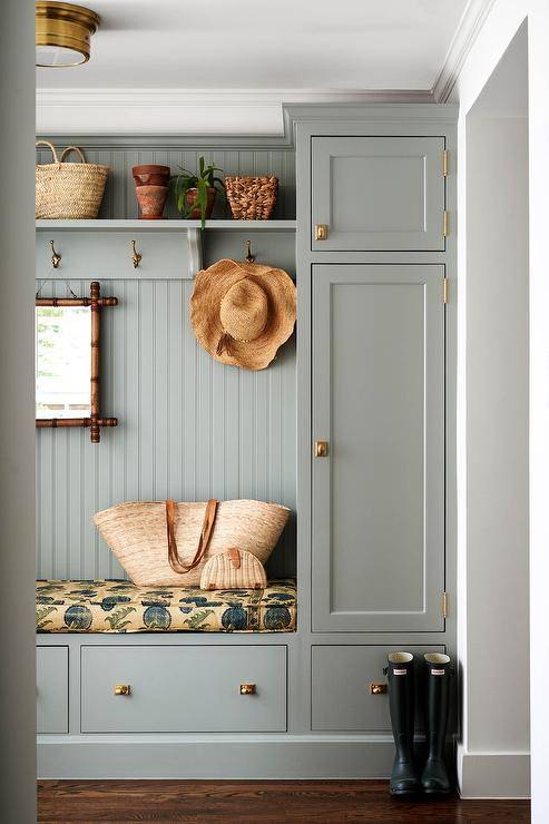 Cottage style mudroom features a built in gray mudroom bench and cabinets with beadboard trim and vintage brass hardware.