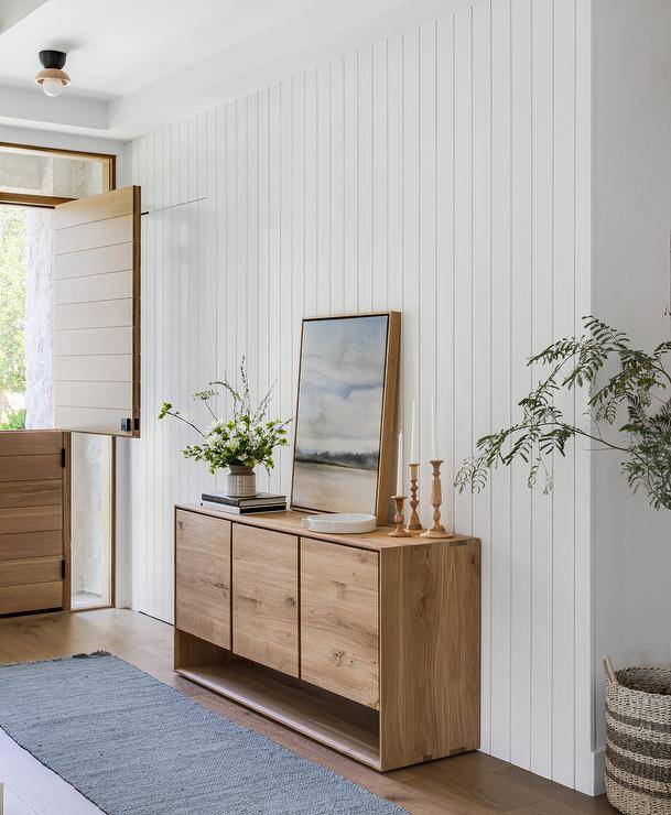 Entryway features a salvaged wood credenza on a white vertical plank wall and a gray rug that leads to a plank Dutch door.