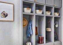 A gray mudroom boasts a row of gray open lockers along with cubbies and drawers adorned with brass pulls.