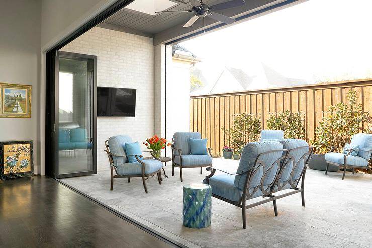 Outdoor patio design displaying glass and metal folding doors opening up to a travertine floor patio with blue seating and accents.