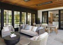 Covered patio features a gray outdoor swivel chair with round black outdoor coffee table, a gray and white outdoor sofa, a gray woven outdoor chair and ceiling heaters on ceiling planks over an gray outdoor dining table with gray rope outdoor dining chairs.