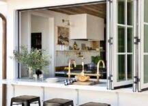 A folding kitchen pass-through windows open to a patio bar seating four black Tolix stools.