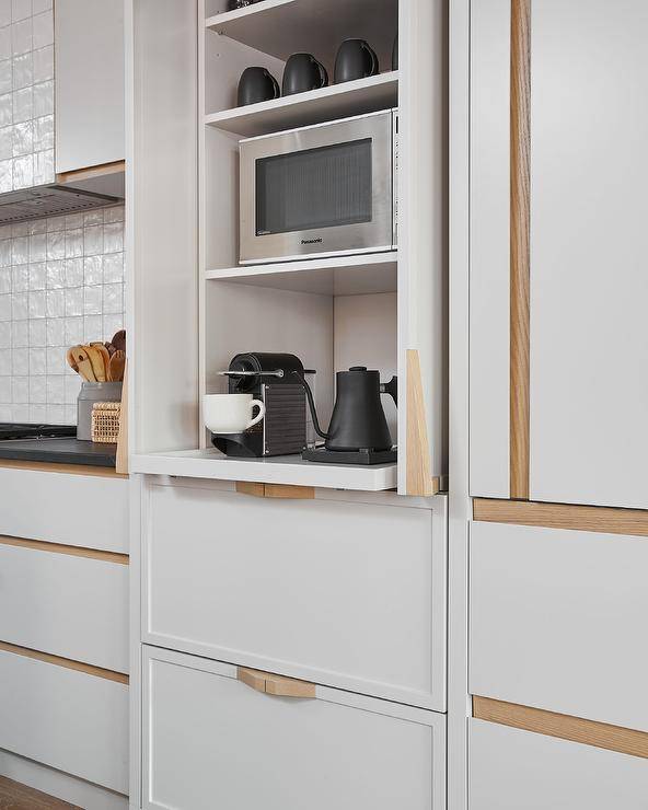 White drawers accented with blond oak hardware are stacked beneath a coffee station boasting white folding doors and pull out shelves.