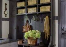 Black cottage style mudroom features a black built-in bench fitted iwth shoe shelves and mounted against black shiplap trim holding polished nickel hooks under stacked black shelves holding woven bins. A gray runner covers black slate floor tiles.
