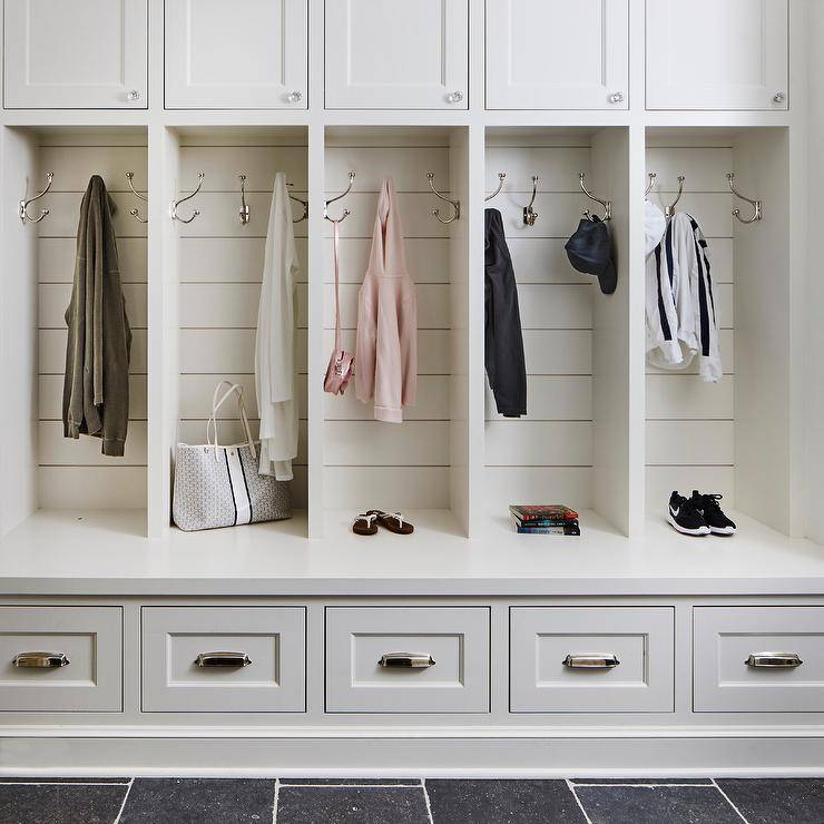Family friendly mudroom features a white quartz built-in bench fitted with storage drawers donning vintage cup pulls and mounted beneath open lockers finished with shiplap trim and polished nickel hooks mounted under white cabinets.
