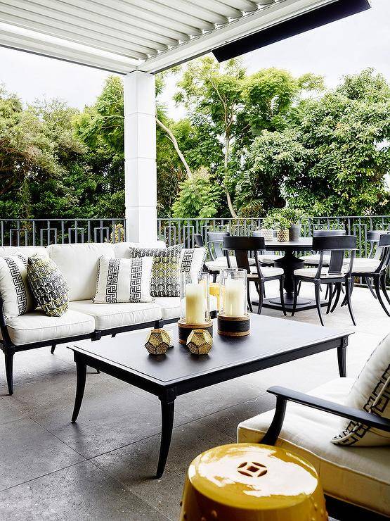 White, black and yellow covered patio design features a black and white outdoor sofa with yellow and black pillows, a black Klismos coffee table and a yellow garden stool.