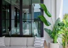 Covered patio features a teak outdoor sectional with gray cushions, a driftwood coffee table, a gray rug and a tall potted plant.