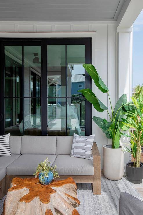 Covered patio features a teak outdoor sectional with gray cushions, a driftwood coffee table, a gray rug and a tall potted plant.