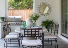 Wrought iron dining chairs sit around an oval marble dining table placed on harlequin pavers beneath a brown plank patio ceiling.