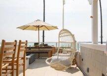 A beach cottage patio features a hanging white rattan chair hung from a white pergola.