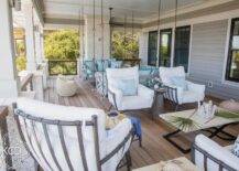 Covered patio features gray swing sofas and chairs, a gray accent chair with white cushion and a black and cream coffee table.