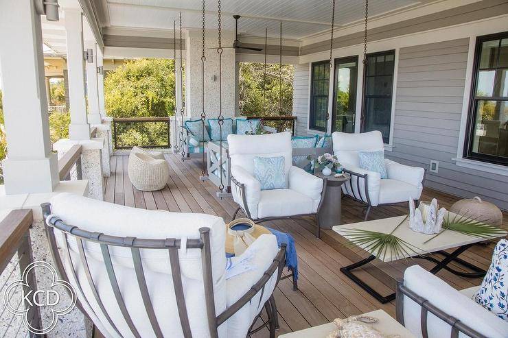 Covered patio features gray swing sofas and chairs, a gray accent chair with white cushion and a black and cream coffee table.