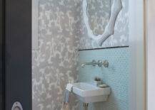 Chic powder room features a black door opening to reveal subtle white and gray floral motif wallpaper highlighting a modern white mirror mounted above an aqua blue glass mini brick tiled backsplash trimmed with black pencil tile framing a mini wall mount sink with modern wall mount faucet.