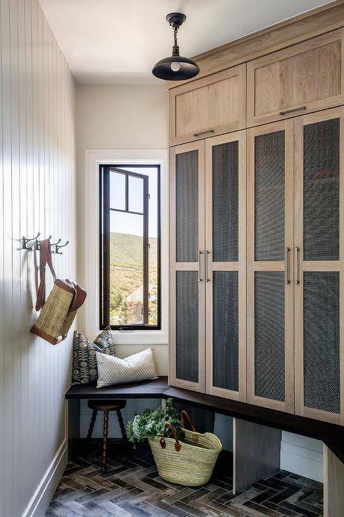 Cabin styled angled mudroom features mesh lockers, a small built in window bench and herringbone floors.