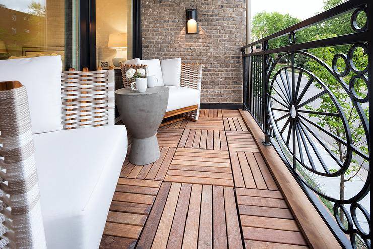 Small transitional balcony made of iron and teak displaying modern wicker club chairs. A concrete accent table is flanked by white upholstered chairs creating stunning patio design.