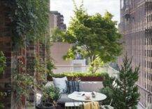 High rise balcony patio furnished with a mint green cafe table and chairs surrounded by lush green plants and a stunning city view.