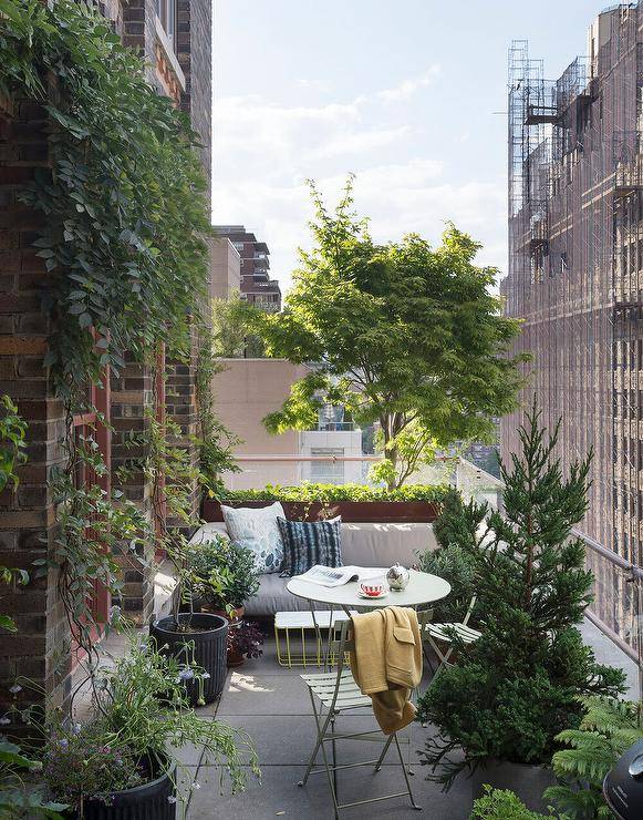 High rise balcony patio furnished with a mint green cafe table and chairs surrounded by lush green plants and a stunning city view.