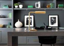 Home office features a brass task lamp that illuminates a black waterfall desk with black velvet chair and black built in shelves with green accents.